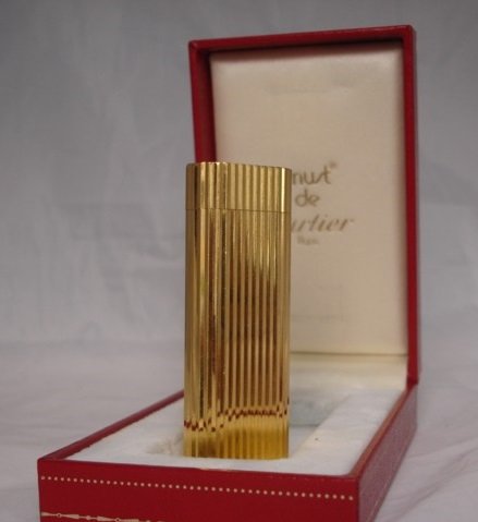 Un mechero Cartier vintage, posiblemente un 'Must de Cartier', mostrando su diseño sofisticado y detalles dorados sobre una superficie de terciopelo, un ejemplo de mechero de lujo icónico.